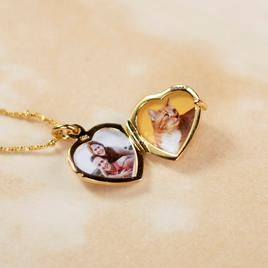 small heart shaped locket in gold lying open with two photos inside