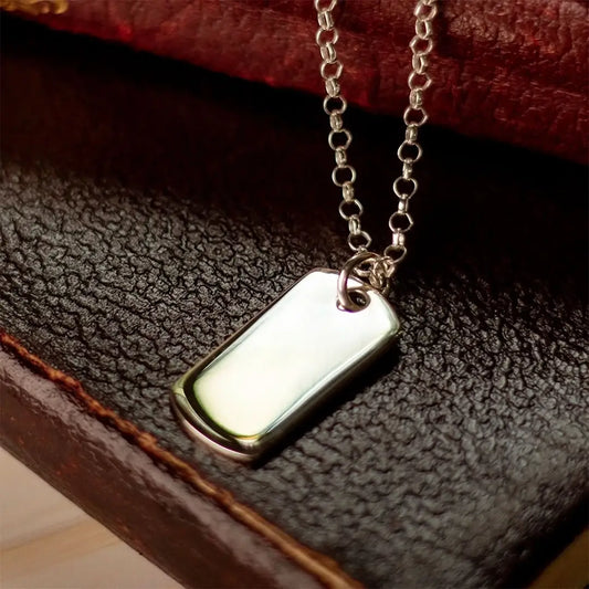 Sterling silver dog tag necklace on belcher chain resting on textured leather, polished blank pendant ready for engraving.