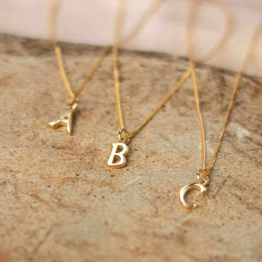 A B C solid 9 carat gold initial necklaces on close curb chains photographed on a sandstone base