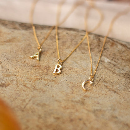 A B C gold initial necklaces photographed on a sandstone base