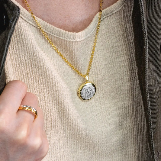 Close-up of a person wearing a gold St Christopher locket necklace with silver St Christopher emblem on a belcher chain