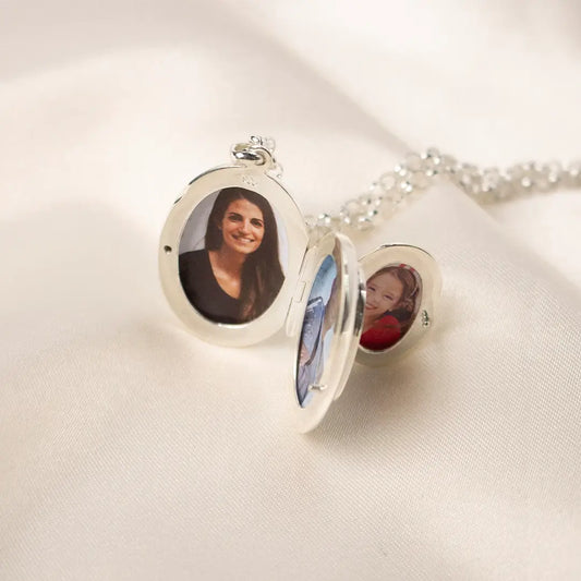 Open sterling silver oval locket necklace showing personalised photos inside, resting on soft cream fabric with delicate silver chain.