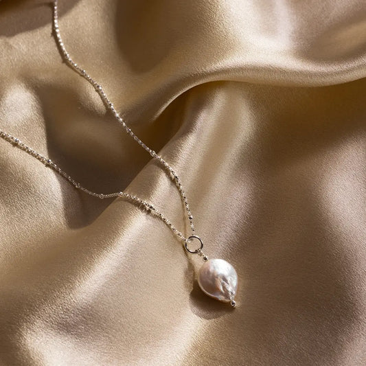 Sterling silver coin pearl pendant necklace on gold satin fabric, highlighting natural freshwater pearl texture