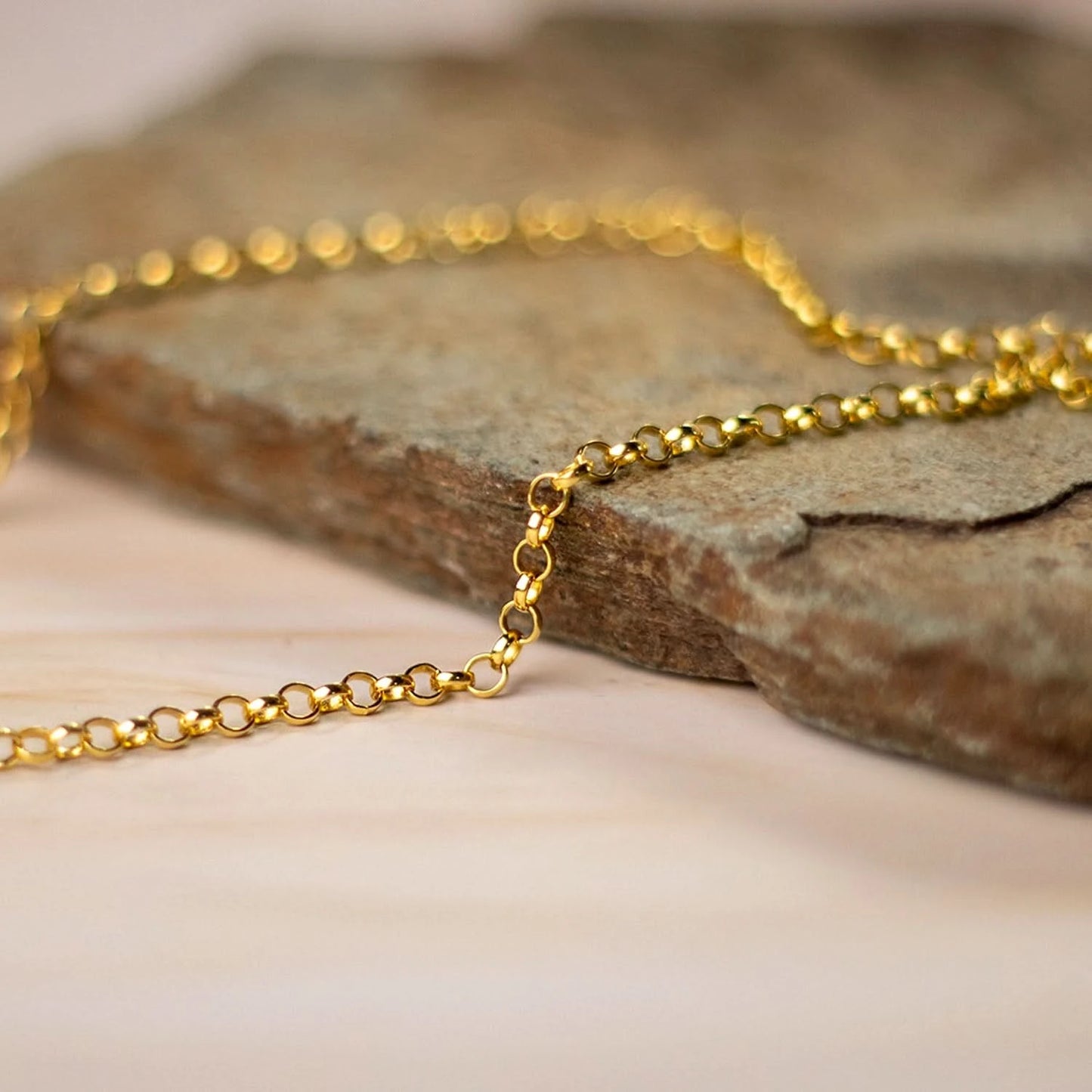 Close-up of delicate gold belcher chain resting on stone surface