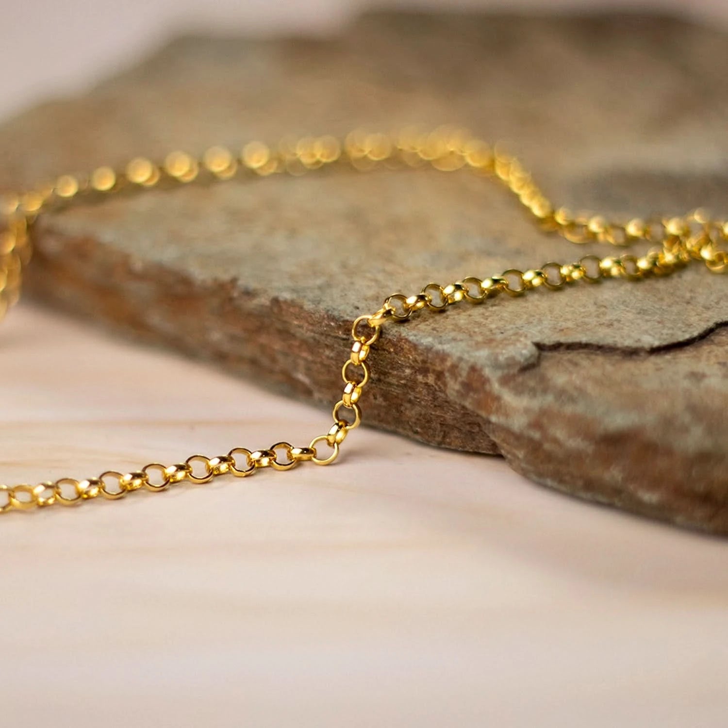 Close-up of delicate gold belcher chain resting on stone surface