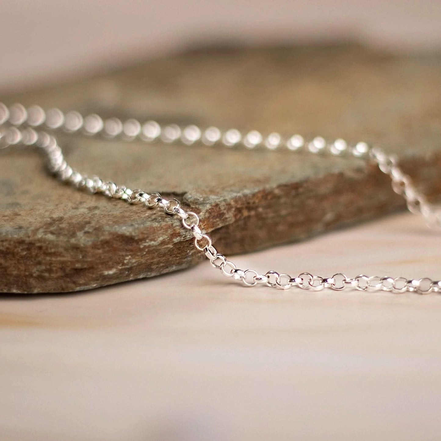 Sterling silver belcher chain necklace resting on natural stone surface, close-up detail of round links