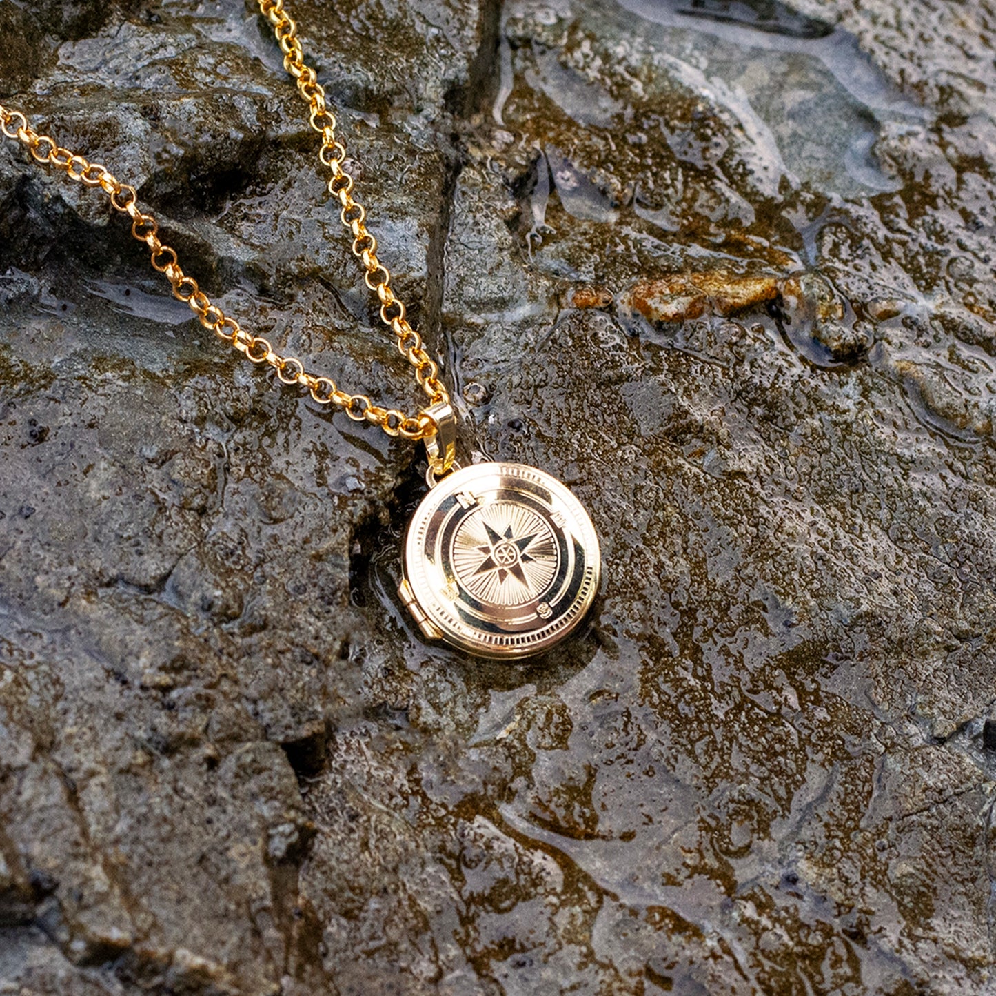 Gold necklace with a compass detail pendant on a stone surface