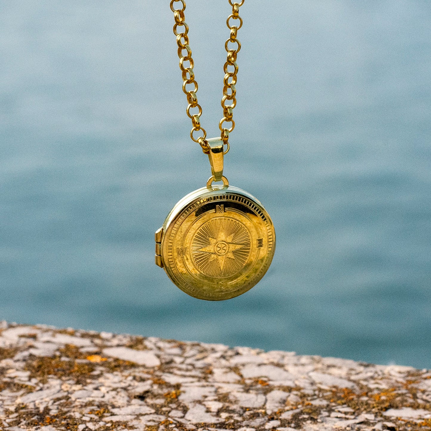 Gold locket necklace on a chain with a blurred water background