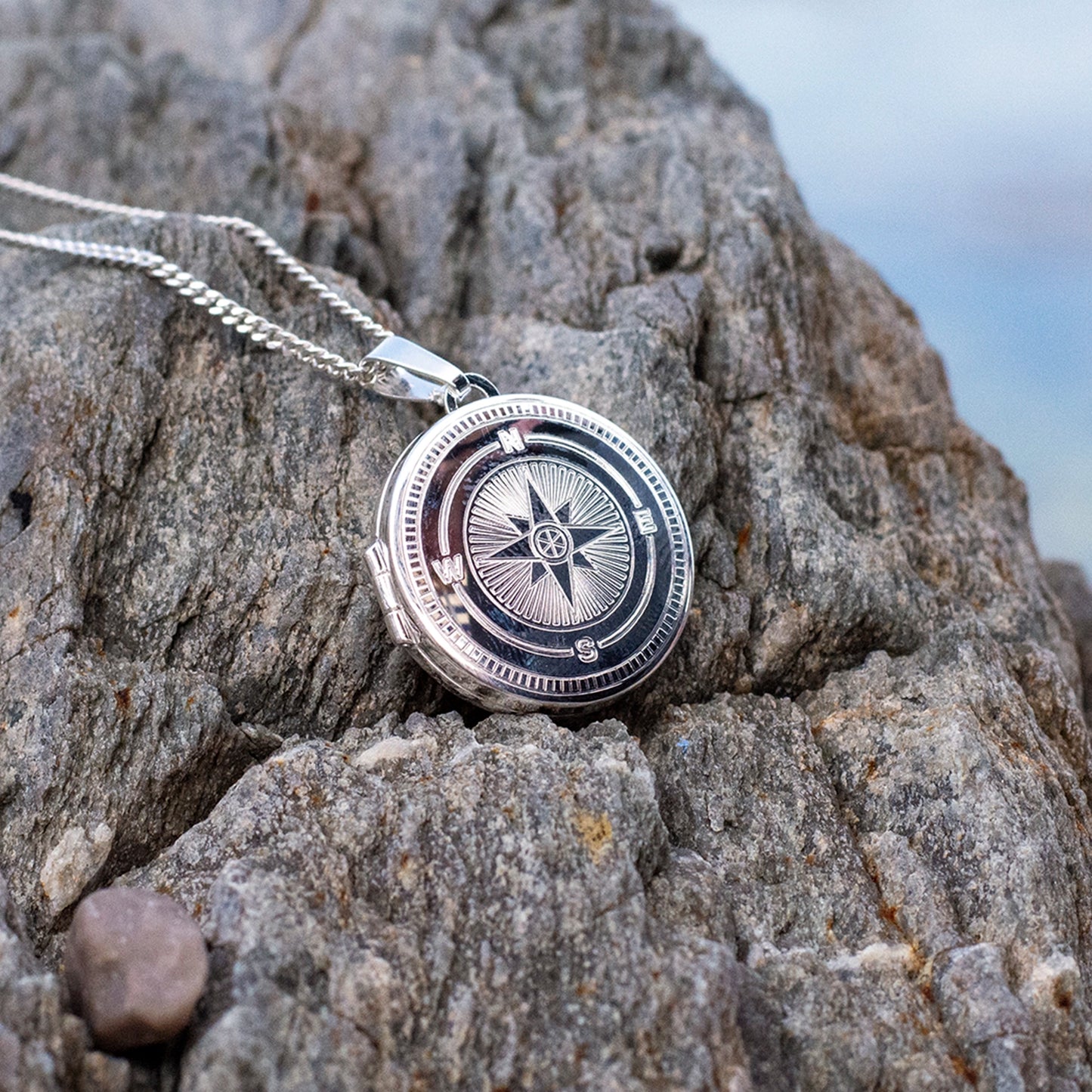 Silver compass pendant necklace on a rocky surface