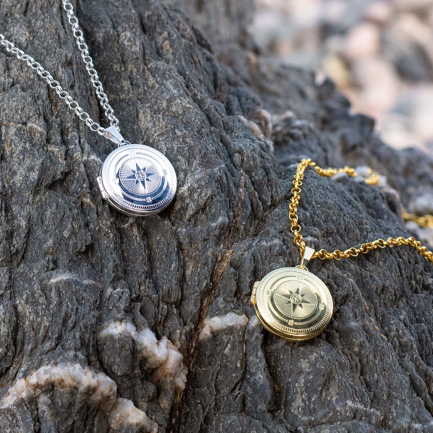 Two necklaces, silver and gold, with compass pendants on a rocky surface