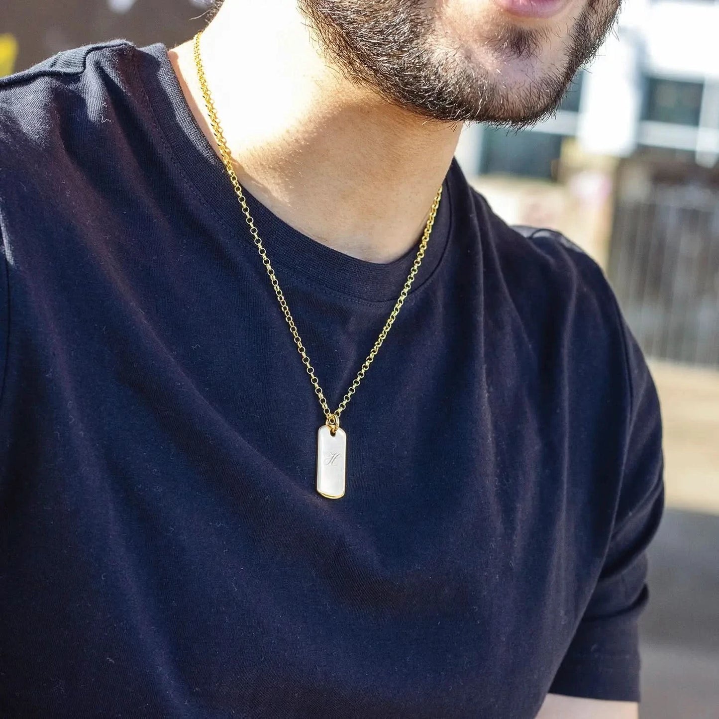 Man wearing a gold dog tag necklace outdoors with black t-shirt