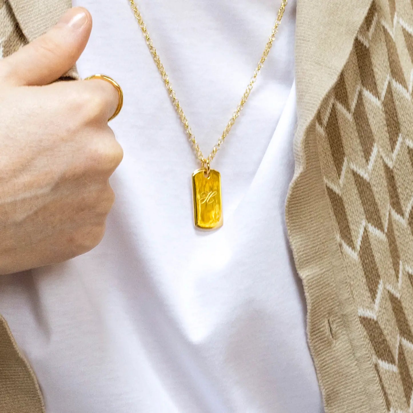 Gold dog tag necklace with a yellow pendant held by a male hand against a white t-shirt