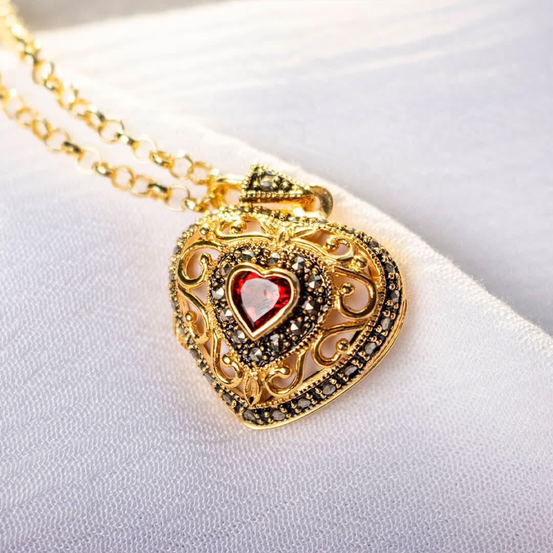 Close-up of gold heart locket necklace with red garnet gemstone and intricate vintage filigree design
