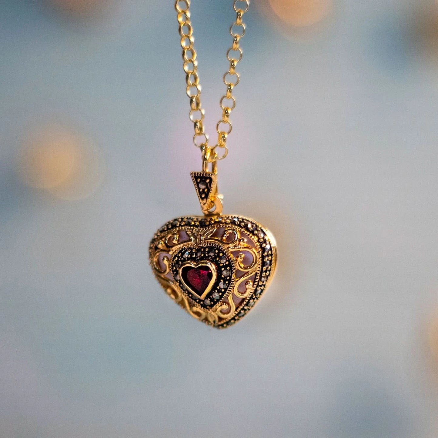 Gold vintage heart locket necklace with red garnet gemstone and ornate filigree design hanging on a gold chain