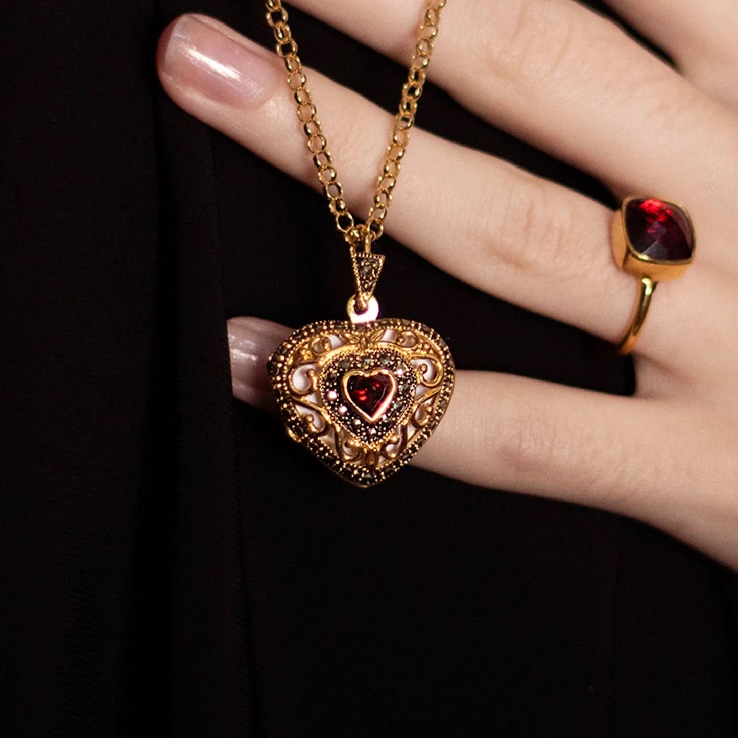 Model wearing ornate gold heart locket necklace with red garnet stone and matching garnet ring