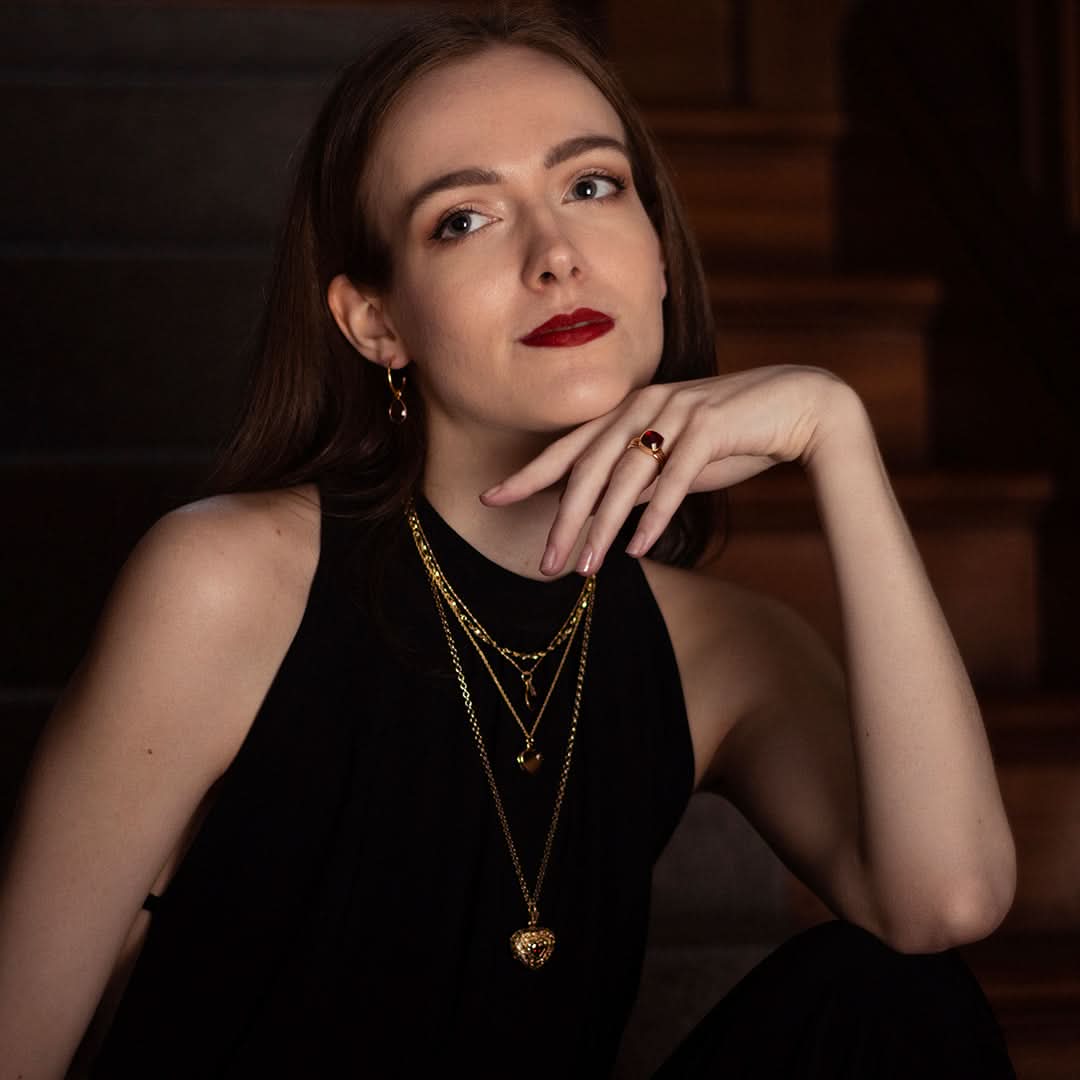 Woman wearing layered gold necklaces with vintage garnet heart locket, ring and earrings