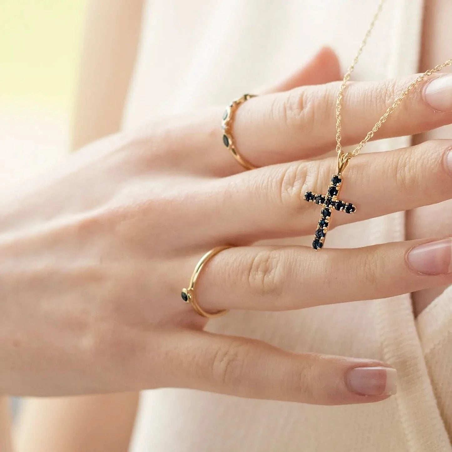 model holding sapphire cross necklace wearing sapphire gold ring