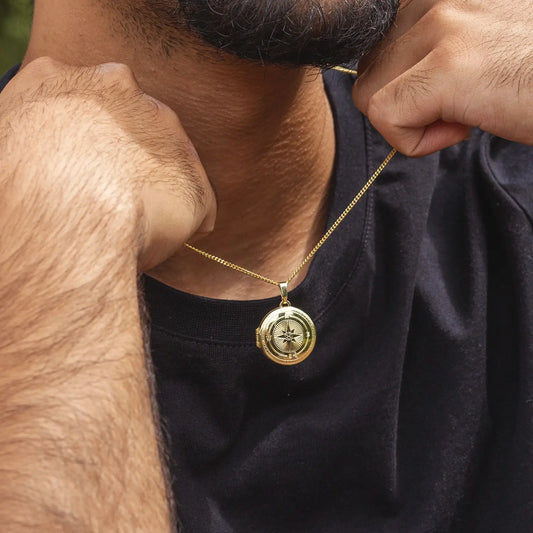 Close-up of a man in a black t-shirt wearing the gold compass locket styled on a curb chain to demonstrate scale and everyday wear