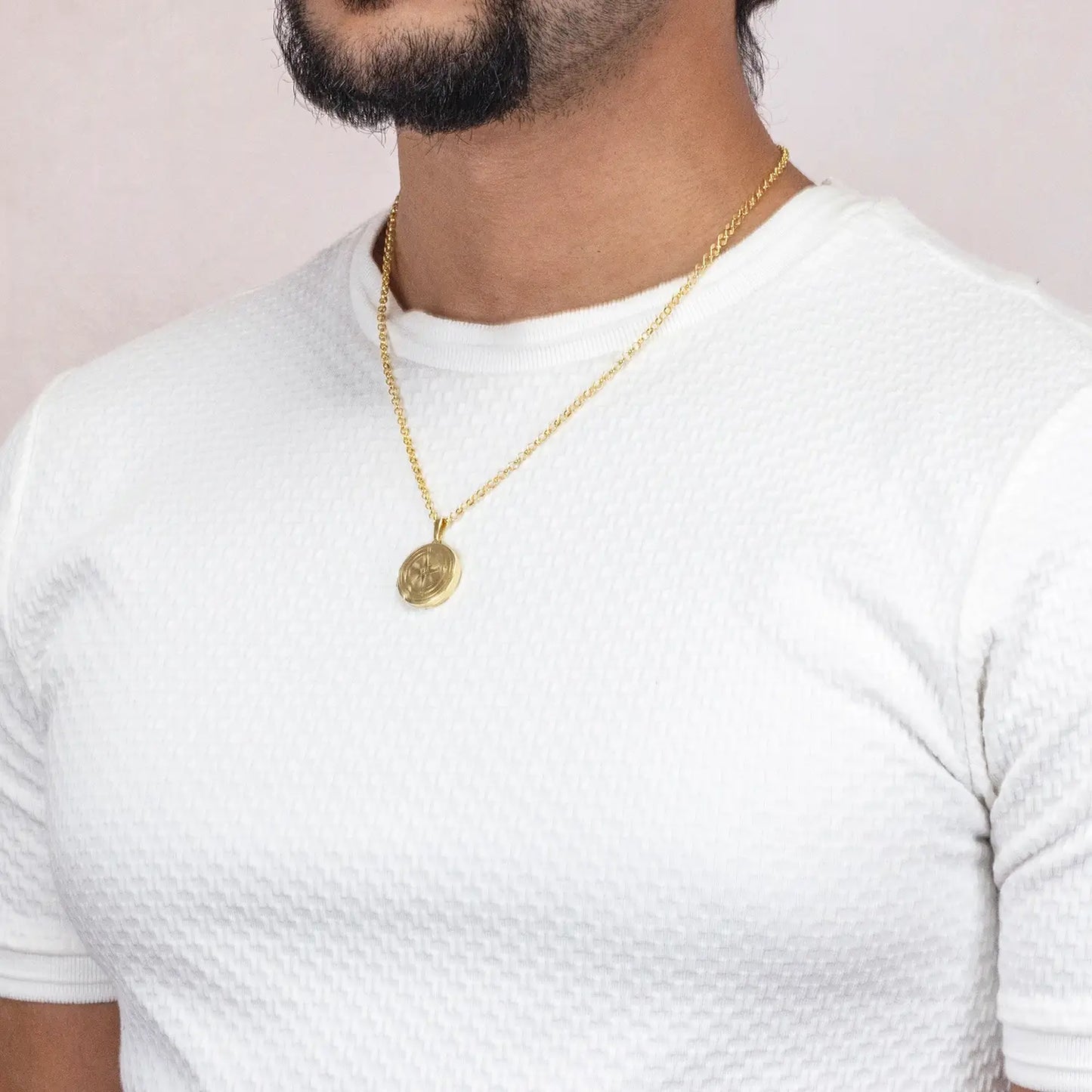 Man wearing a gold compass necklace with a pendant on a plain background