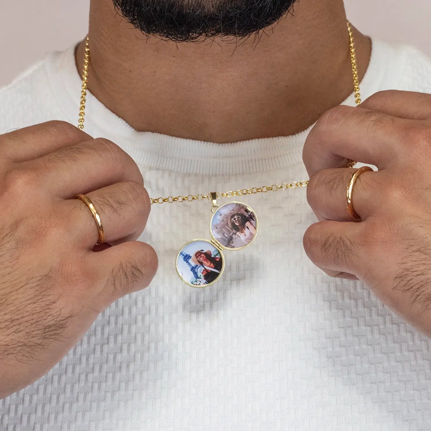 man wearing a gold compass necklace with two round photos, wearing a white shirt