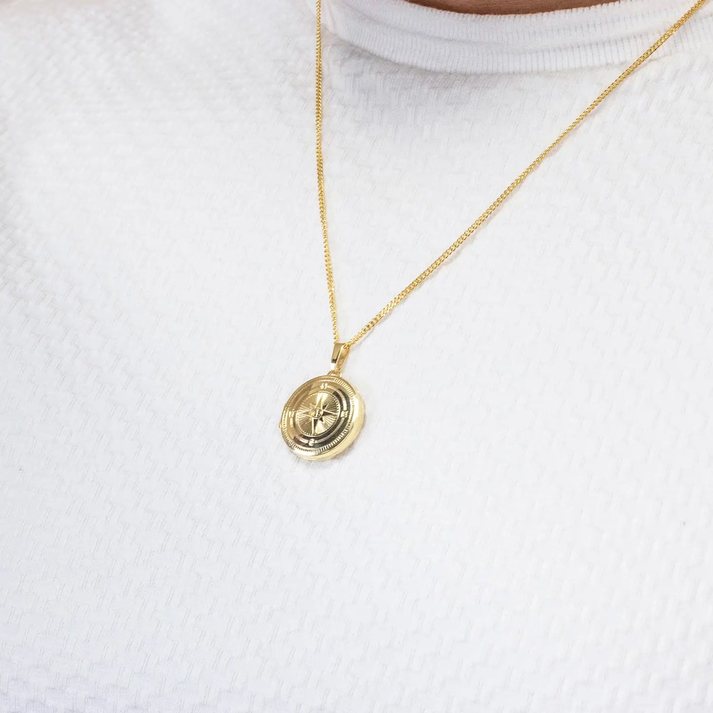 close up of a Gold necklace with a round pendant worn on a white shirt