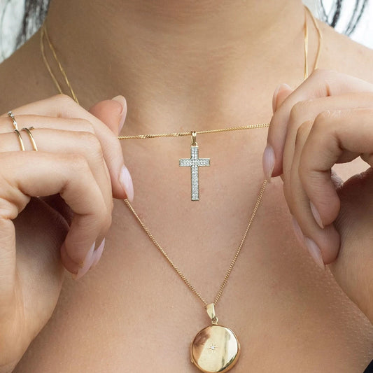 woman wearing gold diamond cross necklace, sturdy gold curb chain, high polish finish, small shiny diamonds, religious Christian pendant for men and women, round diamond gold locket