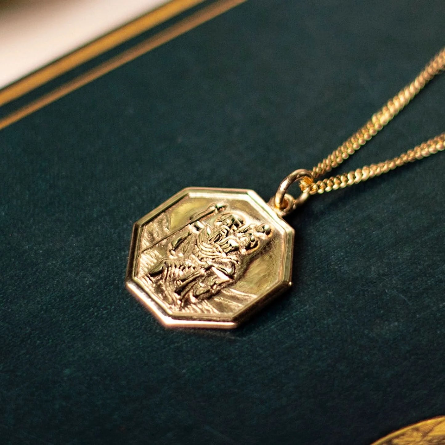 octagonal solid gold st christopher necklace with raised relief on dark green leather book