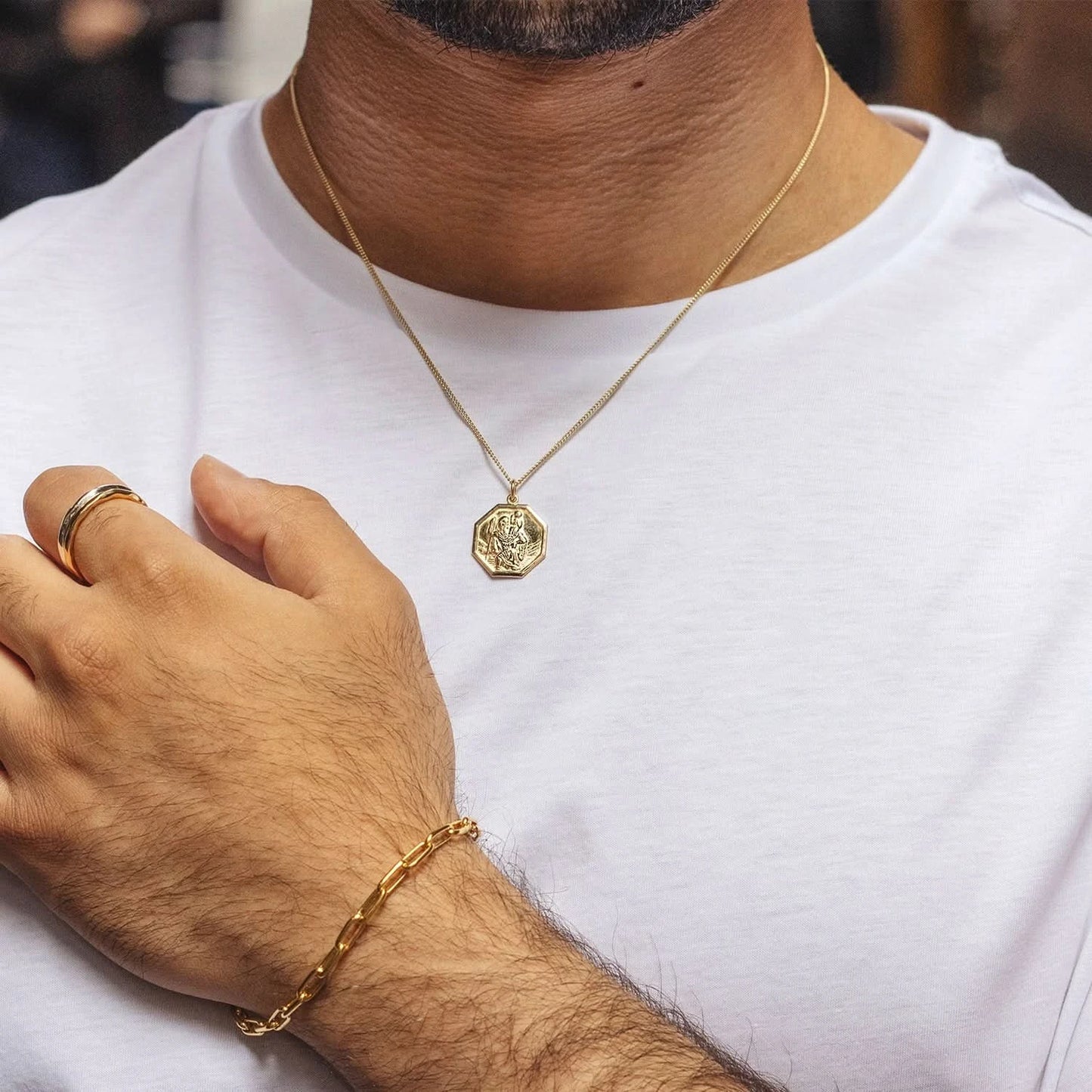 Man wearing gold St. Christopher pendant necklace, gold ring, and gold chain bracelet