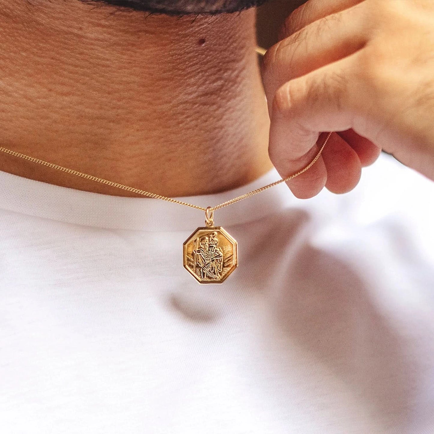 Man wearing gold St. Christopher pendant necklace with octagon frame against a white shirt
