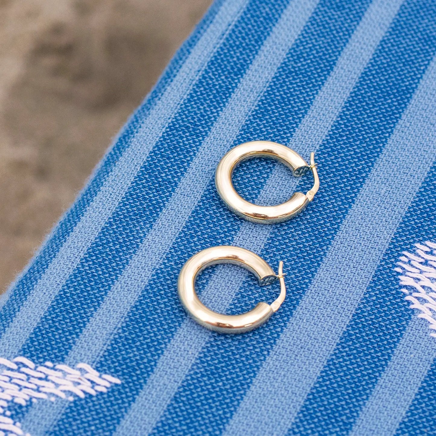 photograph of a large pair of gold hoop earrings on a beach towel