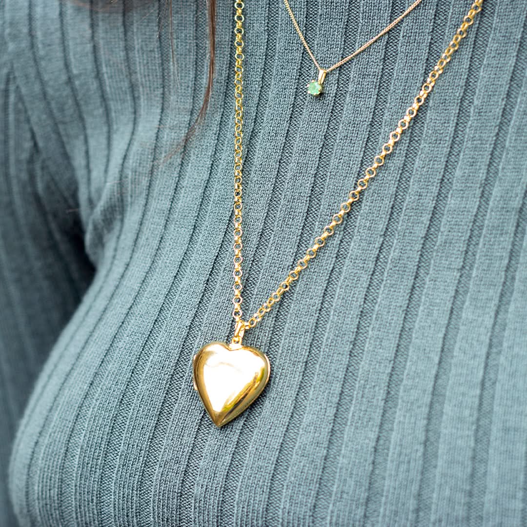Large gold heart locket necklace on model wearing ribbed green top