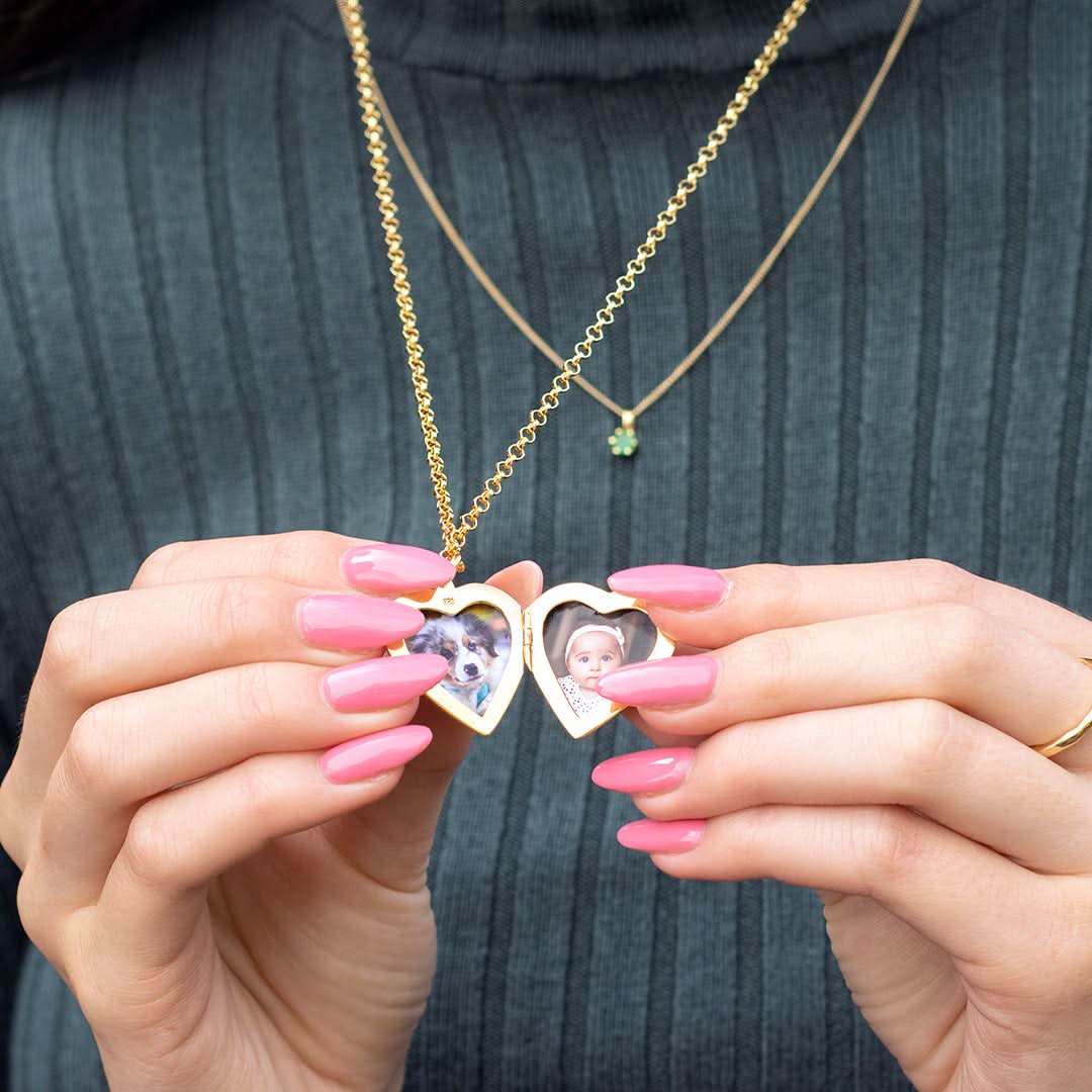 Hands holding an open gold heart locket necklace with photos of a baby and dog inside