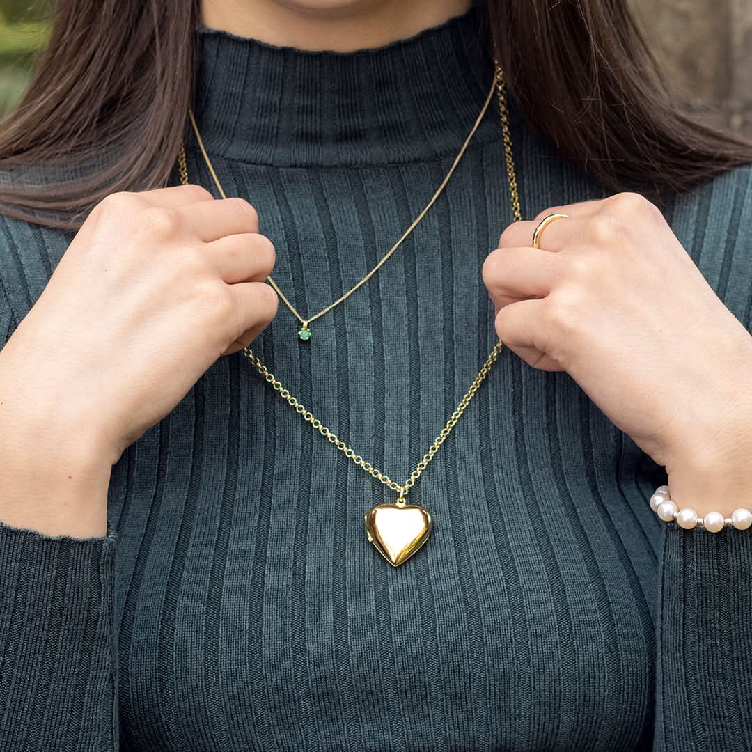 Woman wearing gold heart locket necklace on a Belcher chain layered with green gemstone necklace