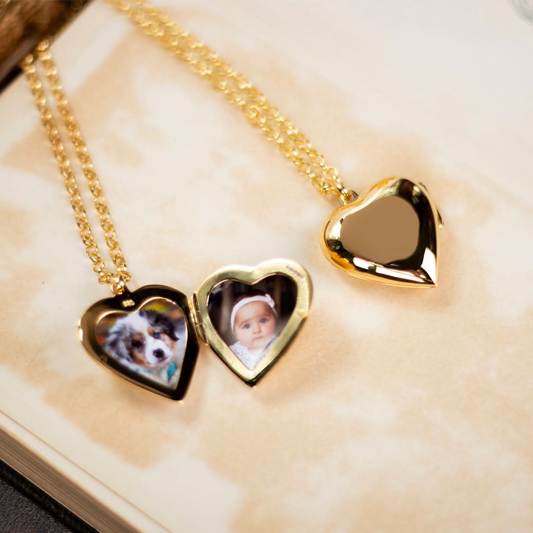 Two gold heart locket necklaces with pet and baby photo inserts on beige book background