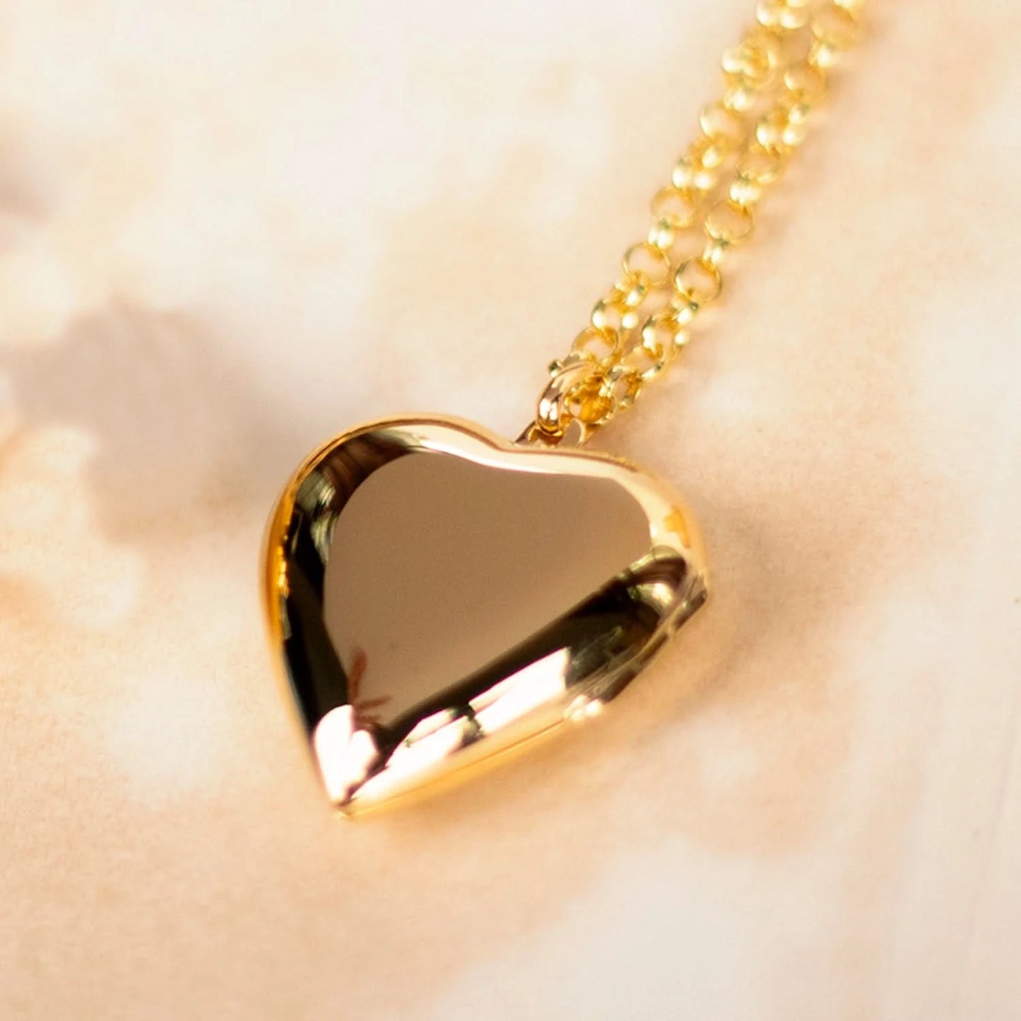 Close-up of gold heart locket necklace with belcher chain on soft neutral background