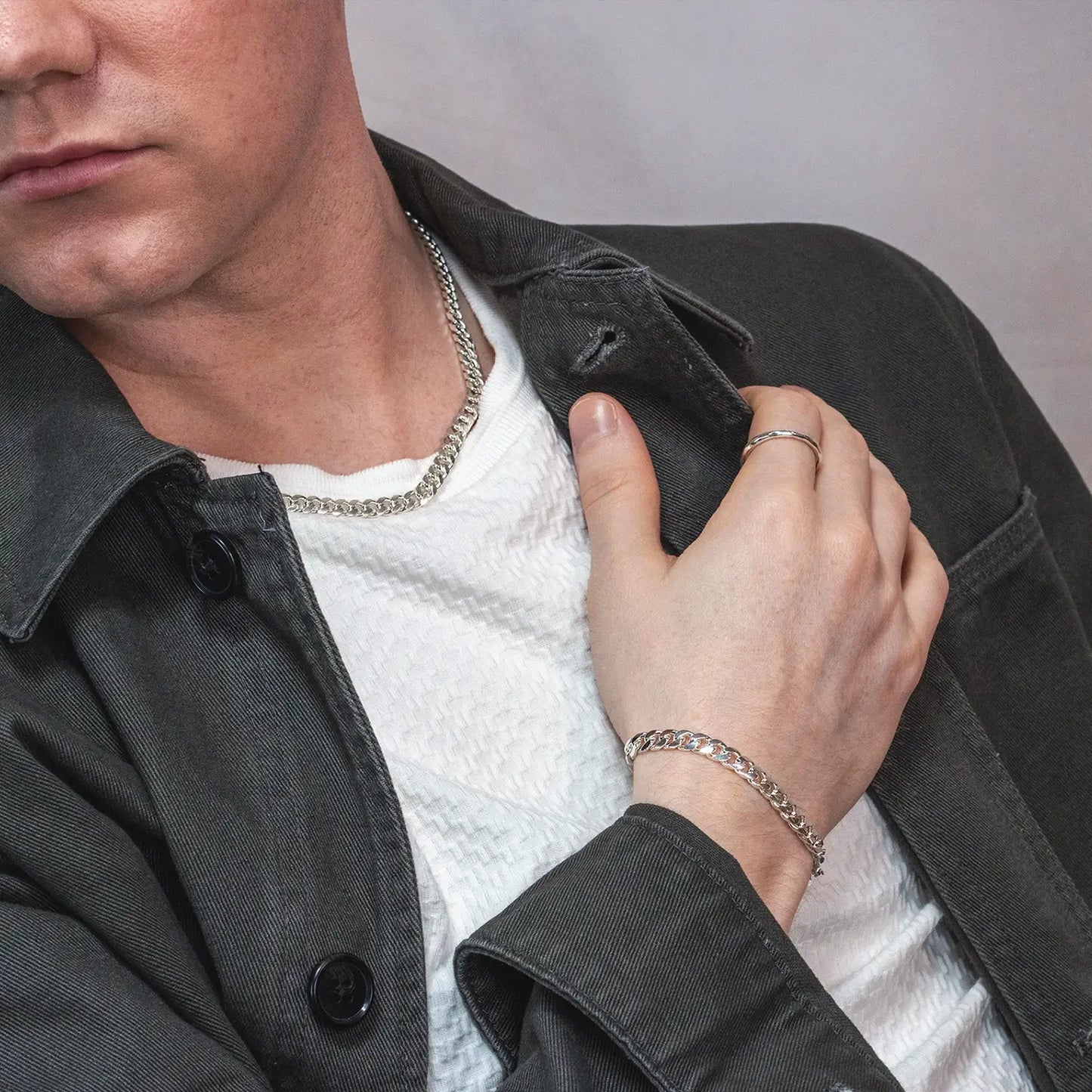 Man wearing a thick sterling silver Cuban chain necklace and bracelet, styled with a white textured shirt and dark jacket