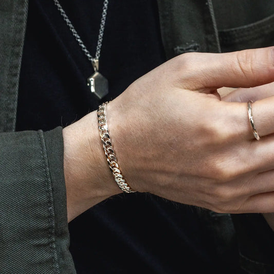 Man wearing a polished sterling silver Cuban link bracelet with a matching chain necklace and silver ring.