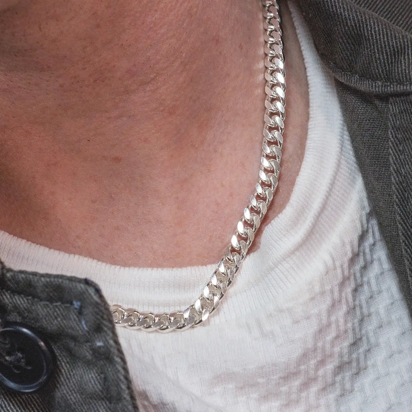 Close-up of a sterling silver Cuban link chain necklace worn with a white textured shirt and dark jacket