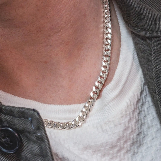 Close-up of a sterling silver Cuban link chain necklace worn with a white textured shirt and dark jacket