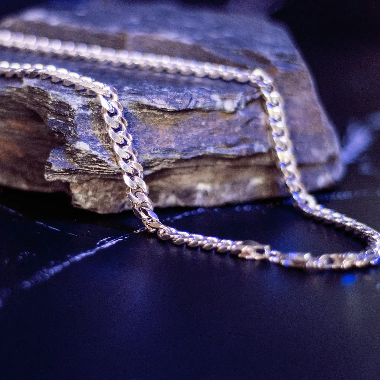 Polished sterling silver Cuban chain draped over a dark stone with reflective blue lighting