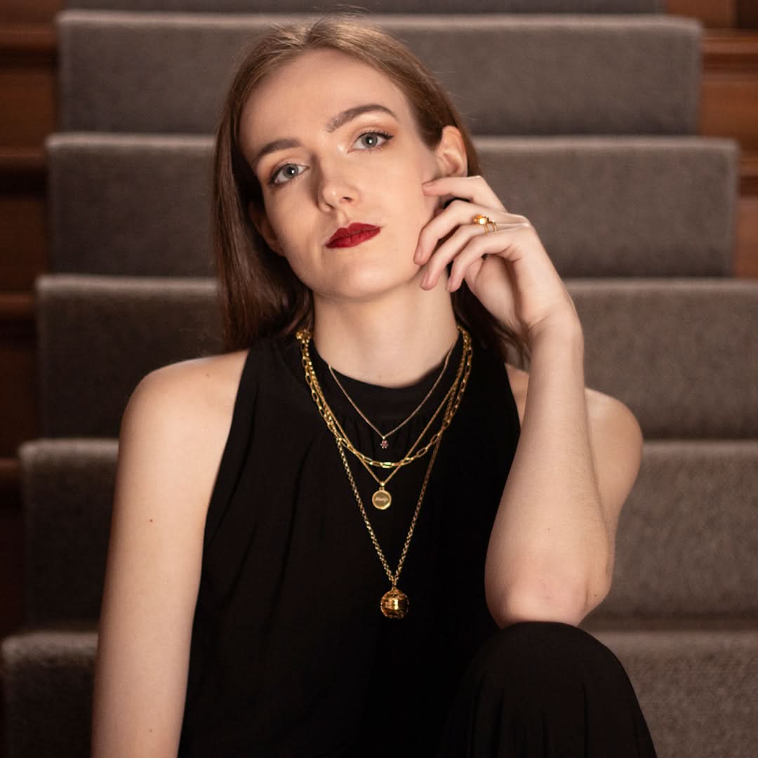 Woman wearing layered gold necklaces including the memory keeper locket while sitting on stairs