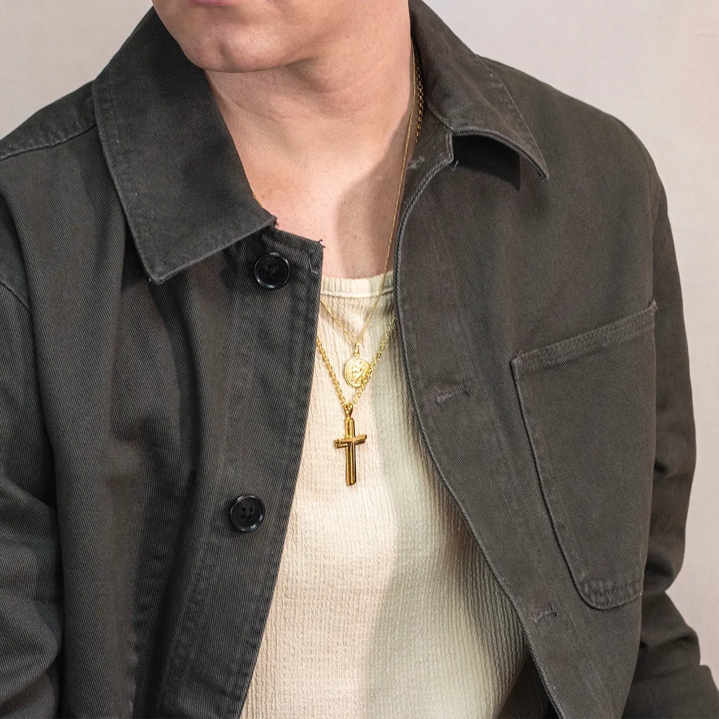 Man wearing a dark jacket with a gold necklace featuring a gold cross pendant.