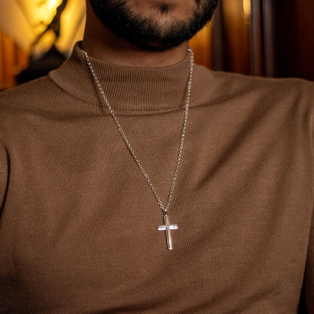 photograph of a heavy weight silver cross necklace on a belcher chain, worn by a male model wearing a brown jumper