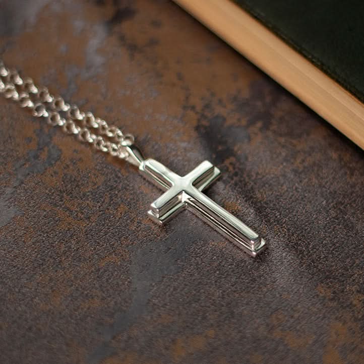 close up photograph of a heavy weight silver cross necklace on a belcher chain, lying against a piece of fabric