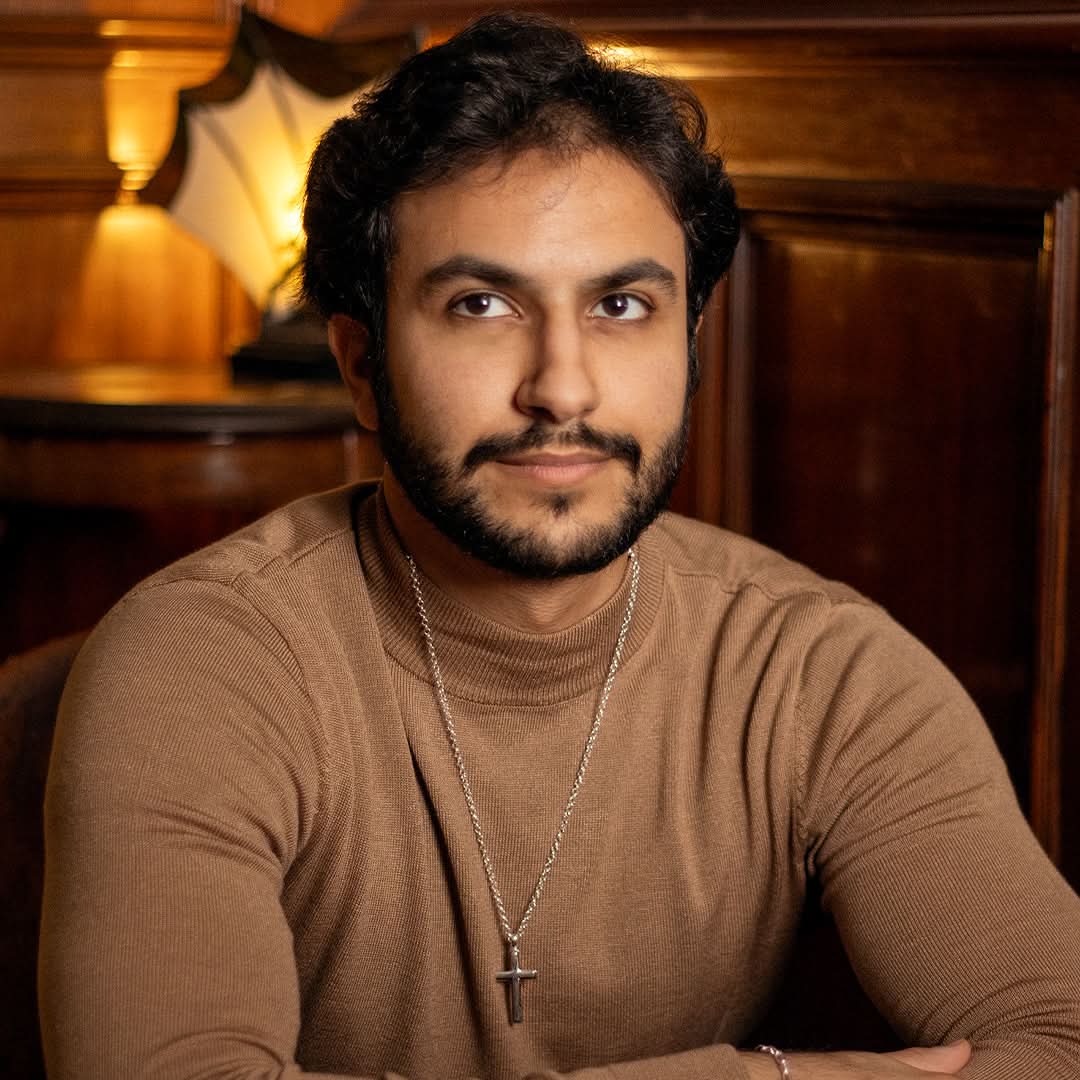 wide view photograph of a heavy weight silver cross necklace on a belcher chain, worn by a male model wearing a brown jumper