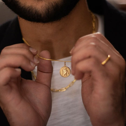 High-quality photo of a men’s gold St. Christopher necklace, featuring a round medallion pendant with intricate detailing. Shown worn on a male model with a black crew neck