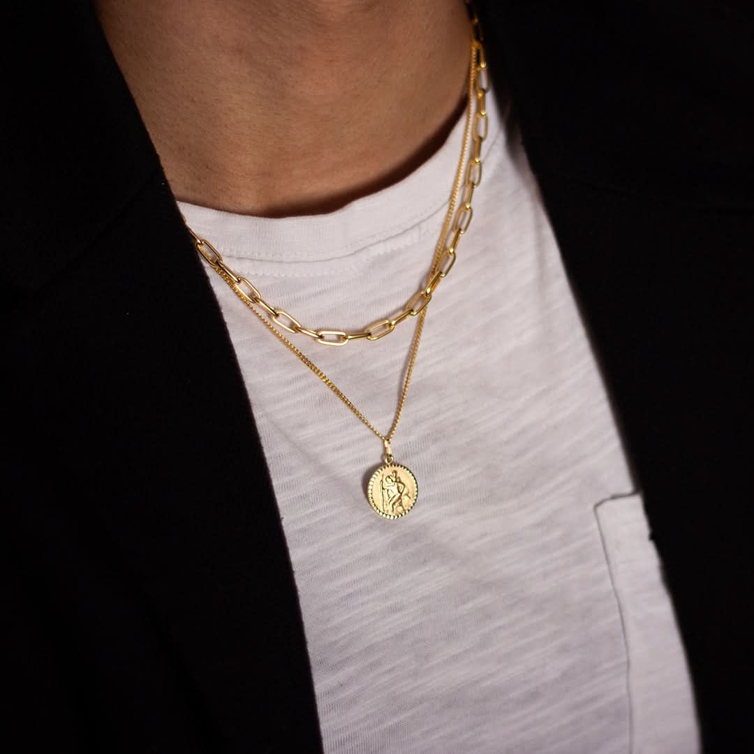 Lifestyle image of a man wearing the gold St. Christopher necklace. The religious pendant sits elegantly over a black shirt, showcasing how the medallion complements casual and formal looks alike