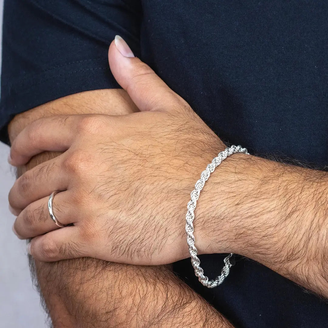 Close up of a man's hand hand wearing a heavy sterling silver rope silver bracelet with a plain background
