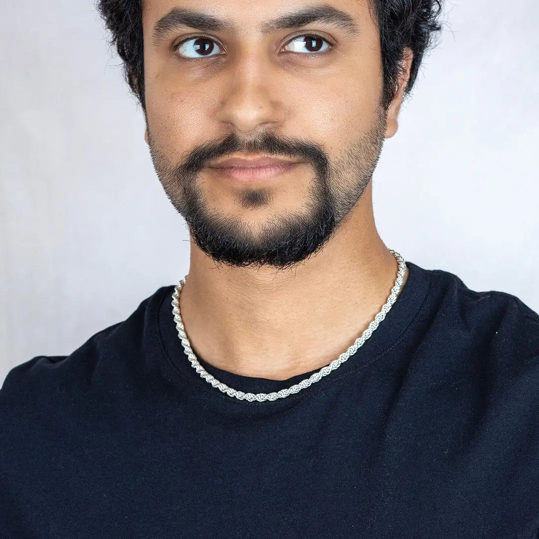 Man wearing a black shirt and heavy sterling silver rope chain necklace against a white background