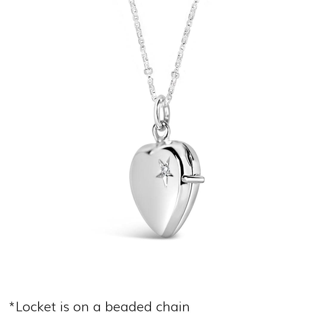 image of a silver heart-shaped locket necklace with a starburst engraving and central diamond. Displayed on a fine beaded silver chain, the locket is photographed against a pure white background